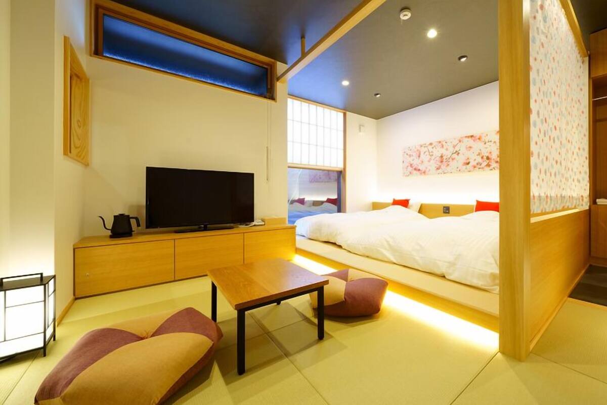 A modern hotel room with a bed, TV, wooden furniture, and a view of the city.