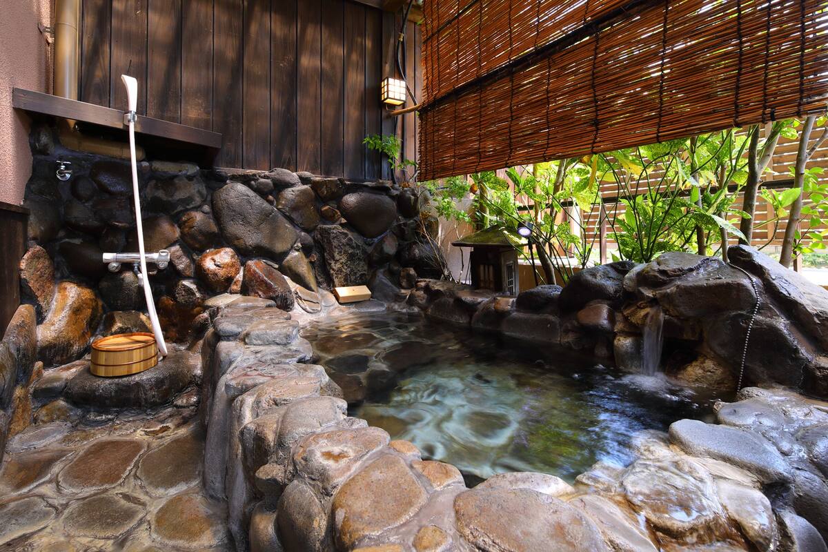A stone hot spring with a wooden structure, a stone wall, and a bamboo fence.