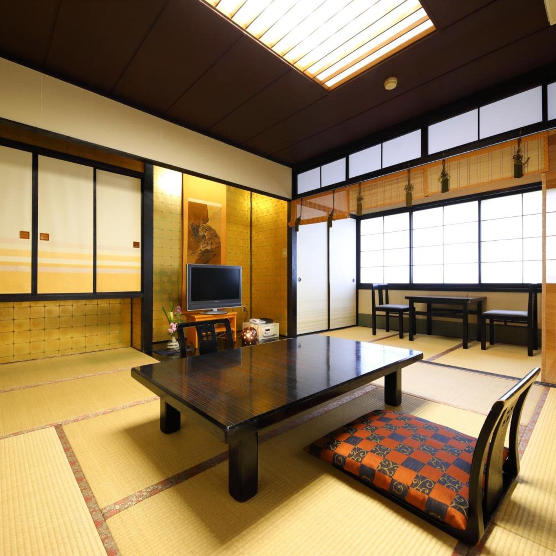 Una habitación japonesa tradicional con suelo de tatami, una mesa baja, un televisor y puertas correderas.
