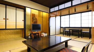 Una habitación japonesa tradicional con suelo de tatami, una mesa baja, un televisor y puertas correderas.