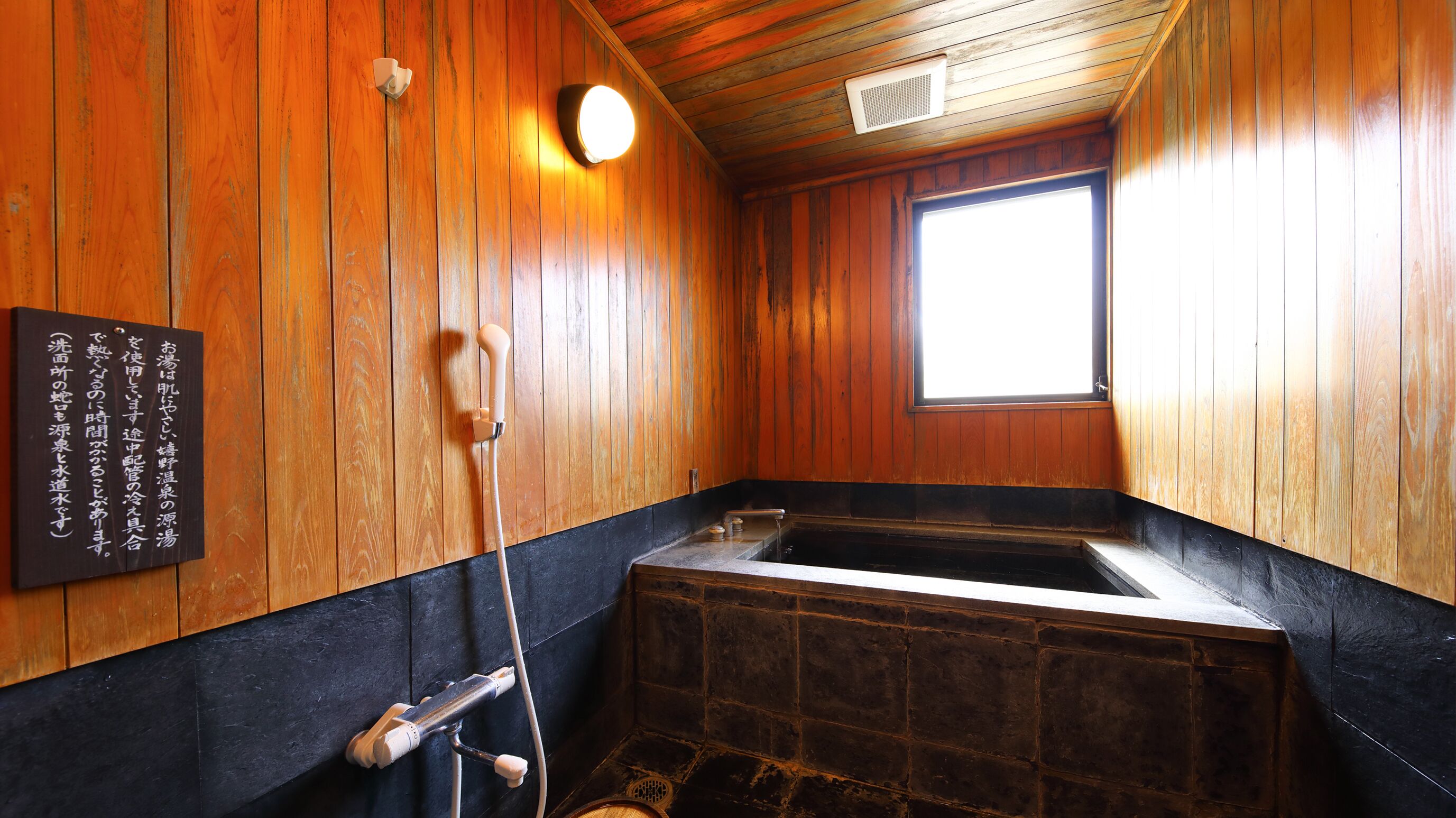 A wooden interior with a stone bathtub, a wooden bench, and a window.