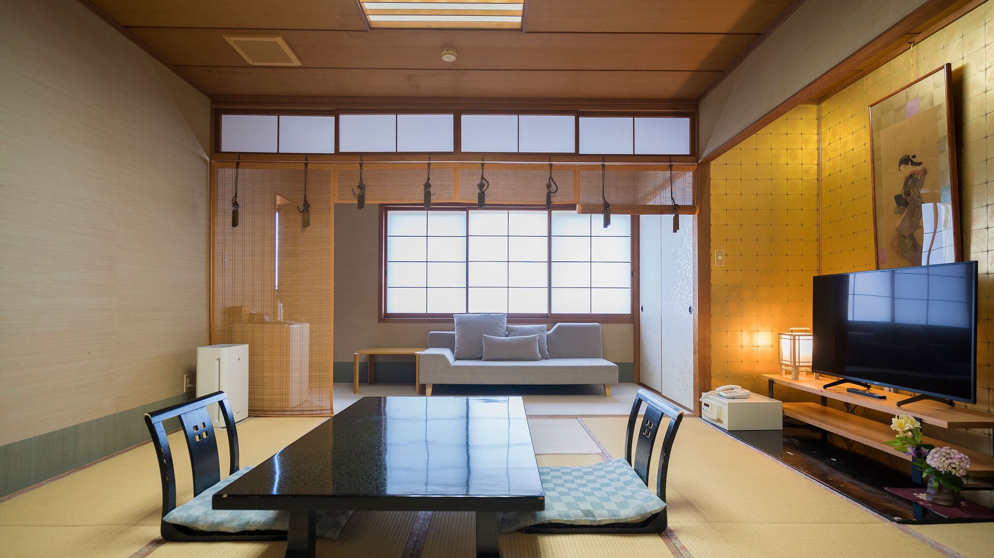 A traditional Japanese-style room with tatami flooring, a low table, a sofa, and a television.