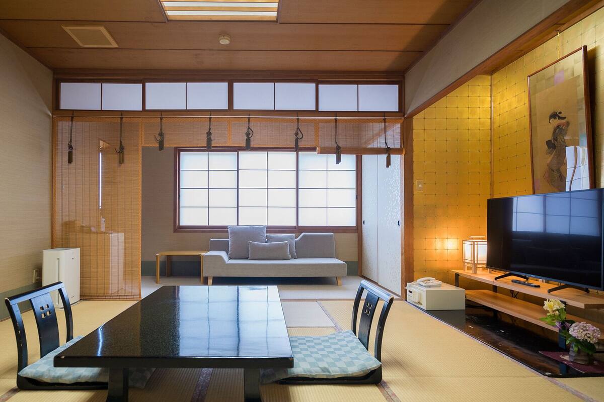 A traditional Japanese-style room with tatami flooring, a low table, a sofa, and a television.