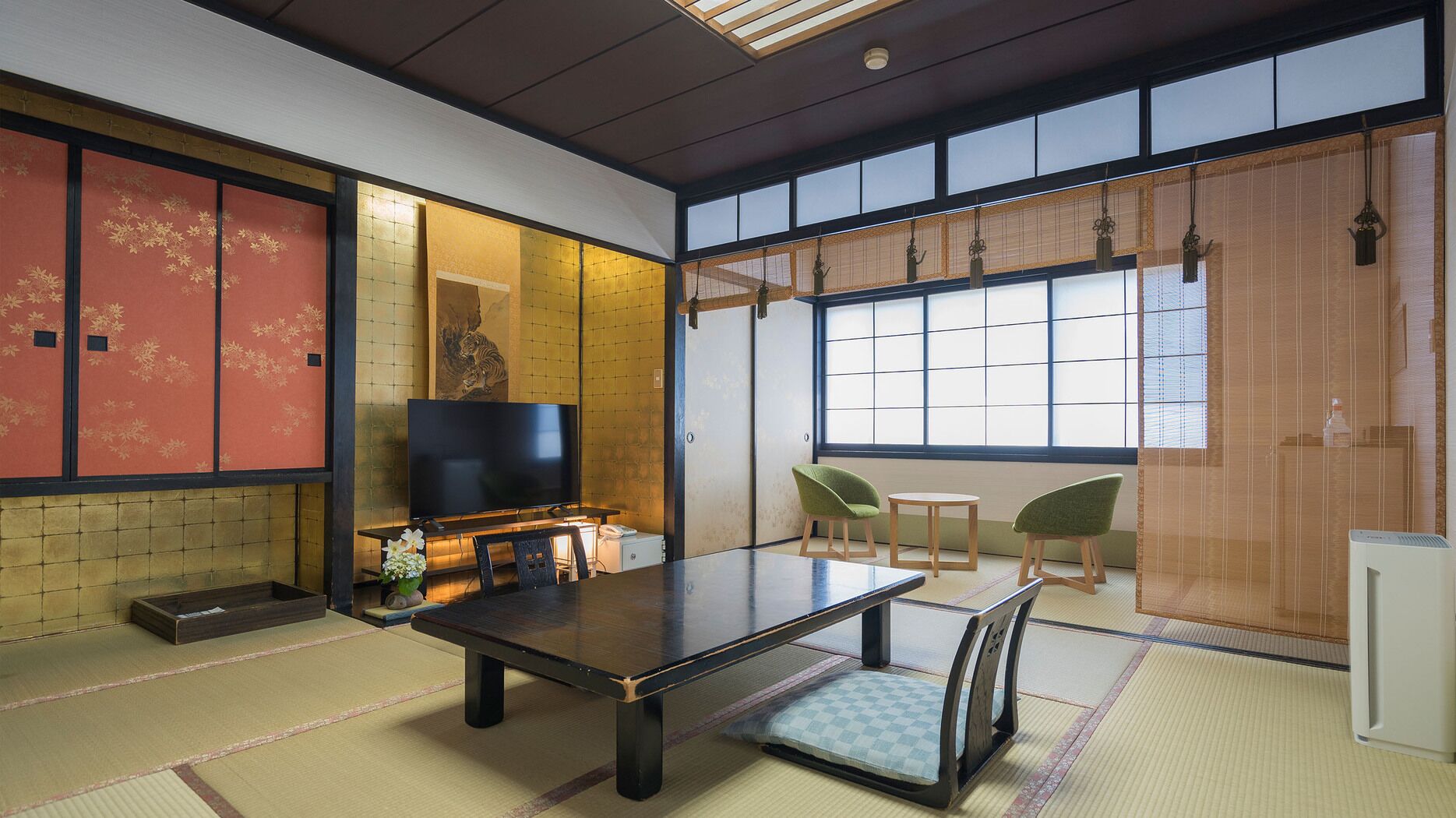 A traditional Japanese room with tatami flooring, a low table, chairs, a television, and sliding doors.