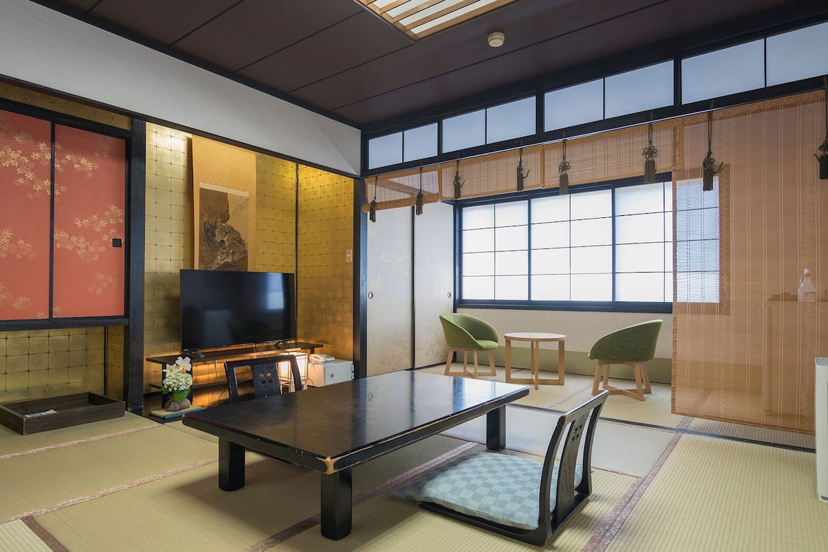 A traditional Japanese room with tatami flooring, a low table, chairs, a television, and sliding doors.