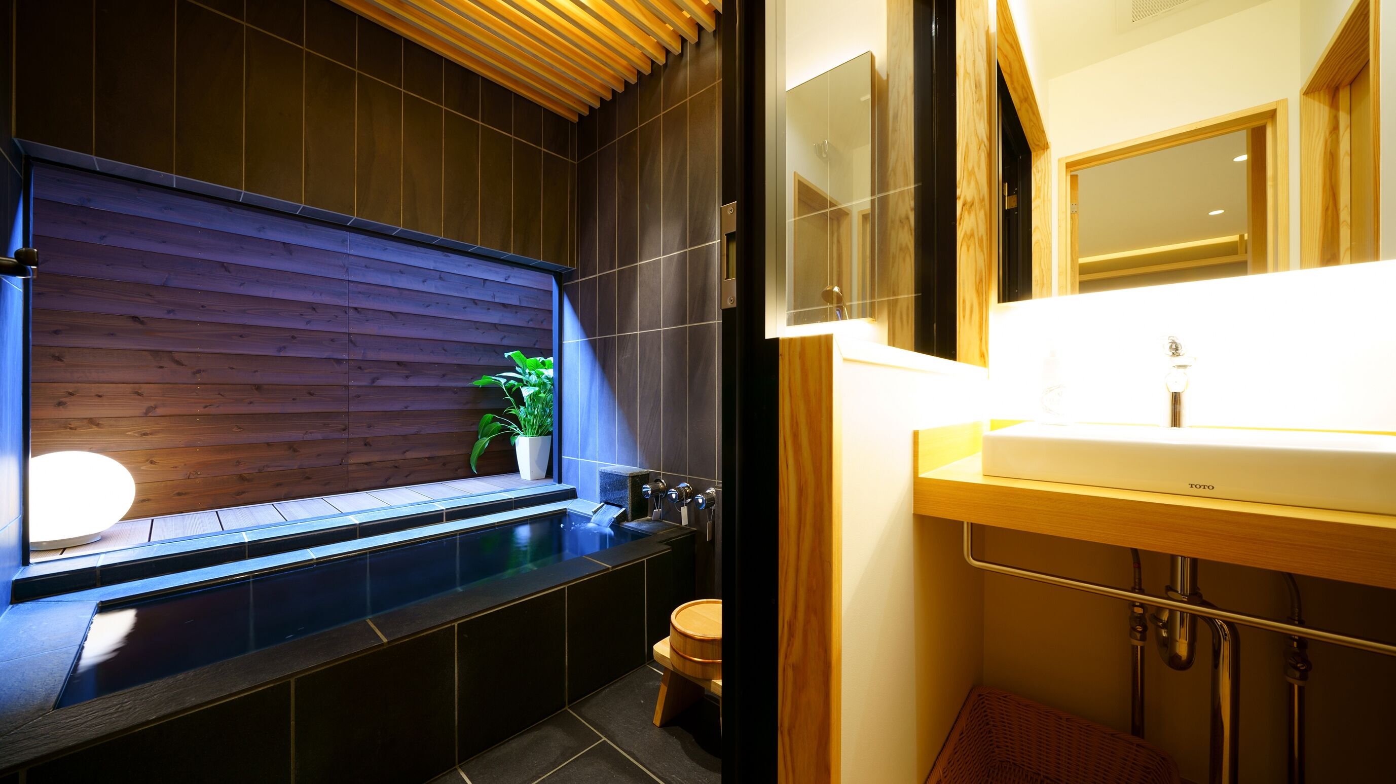 A modern bathroom with a wooden panel wall, a built-in bathtub, a sink with a mirror, and a toilet.