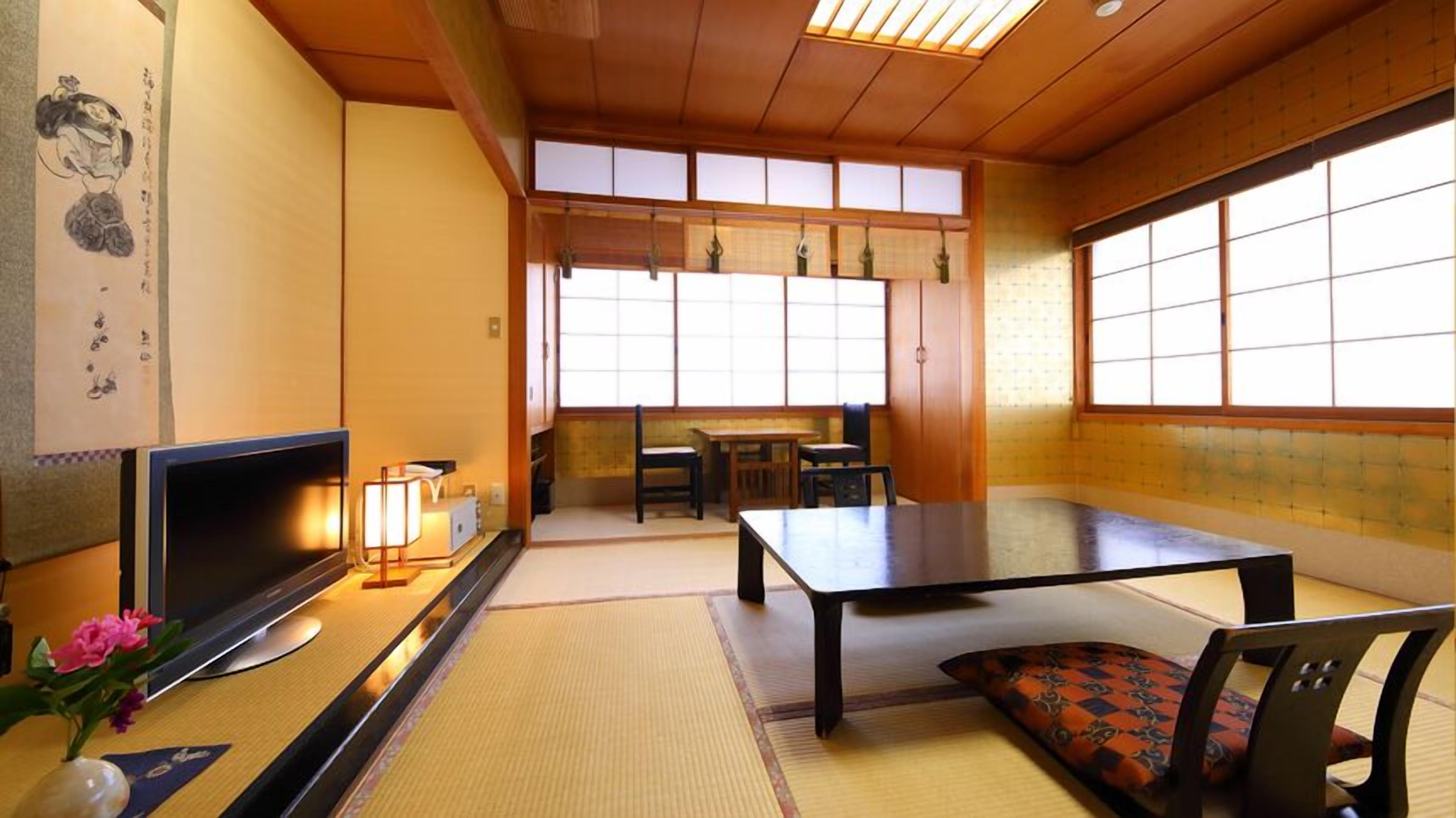 A traditional Japanese room with tatami flooring, a television, a table, and a sofa.