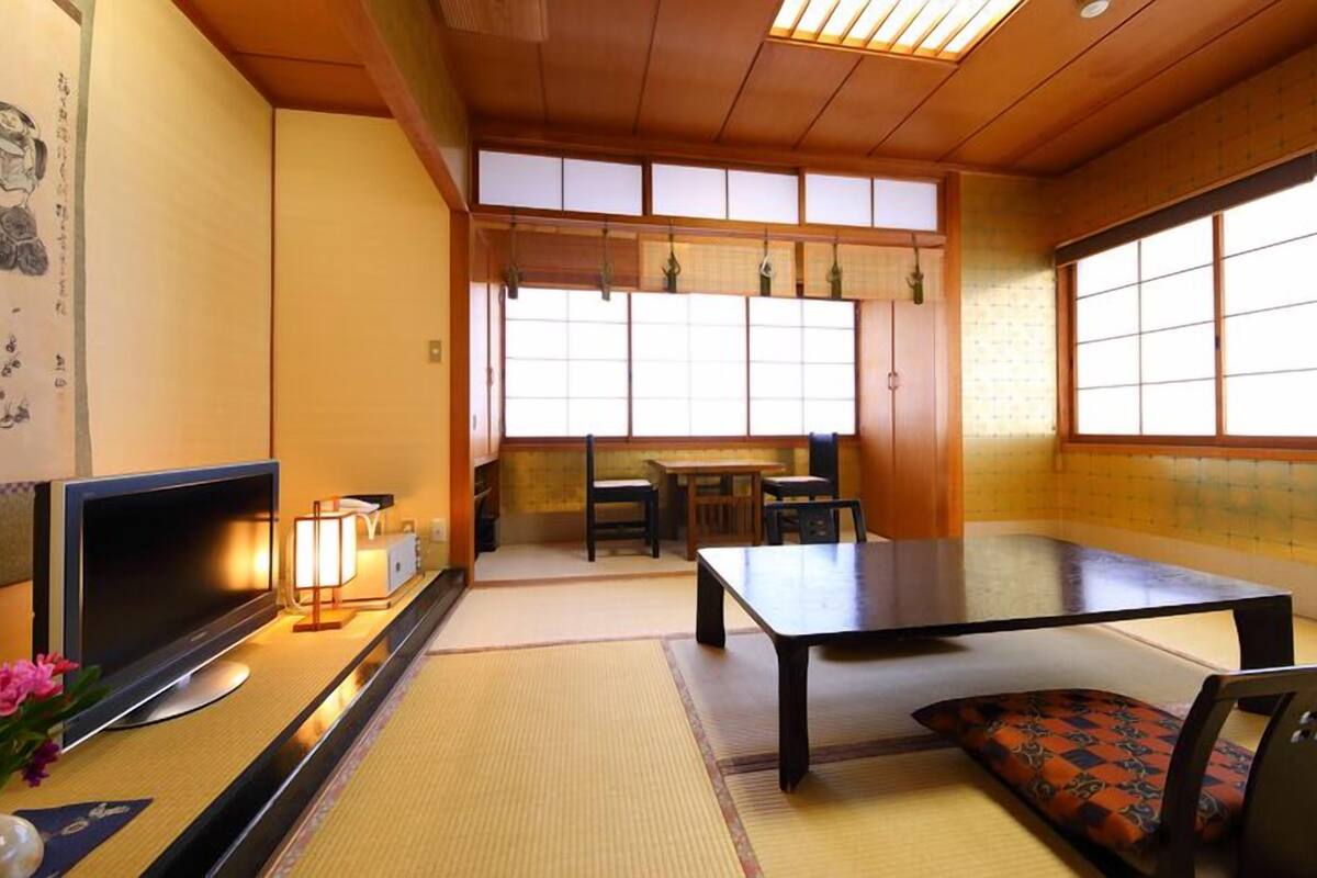 A traditional Japanese room with tatami flooring, a television, a table, and a sofa.