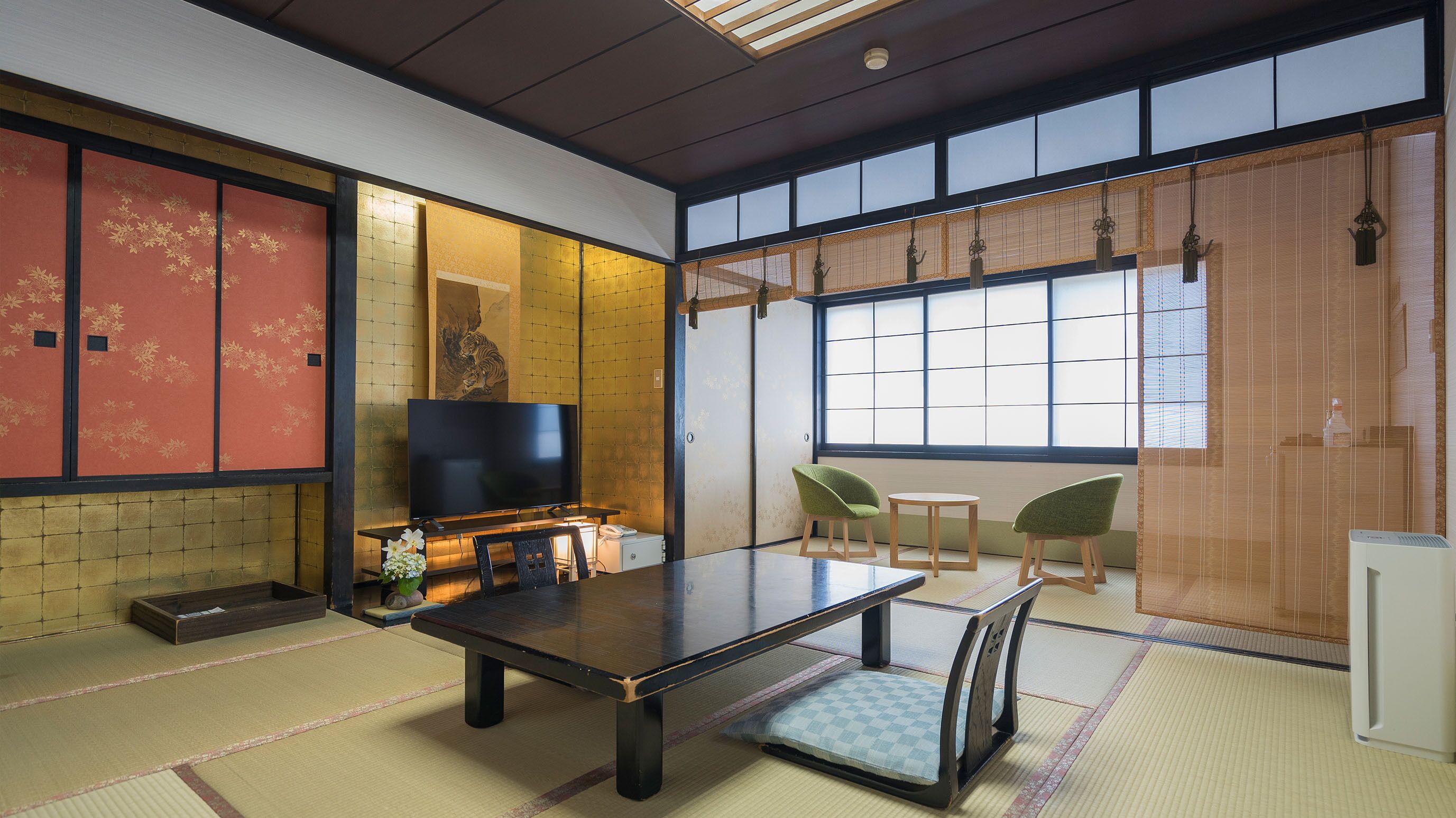 A traditional Japanese room with tatami flooring, a low table, chairs, a television, and sliding doors.