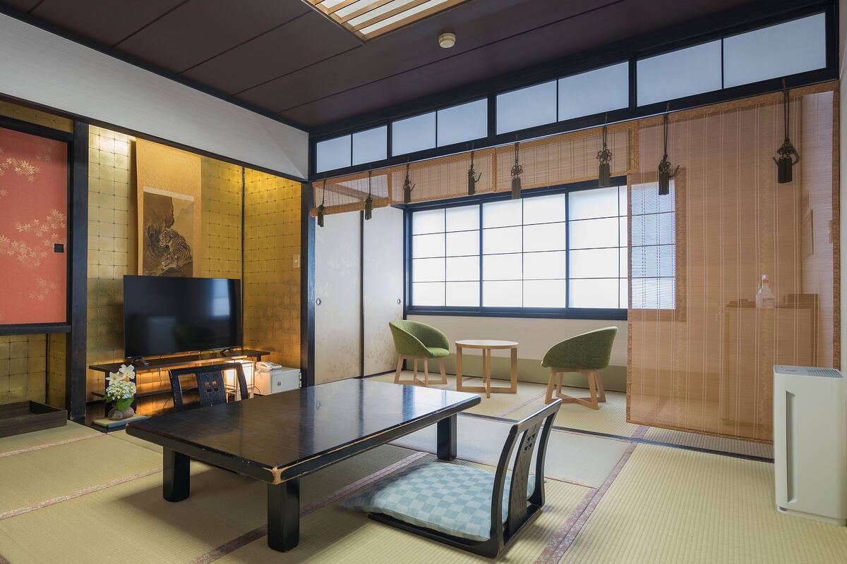 A traditional Japanese room with tatami flooring, a low table, chairs, a television, and sliding doors.