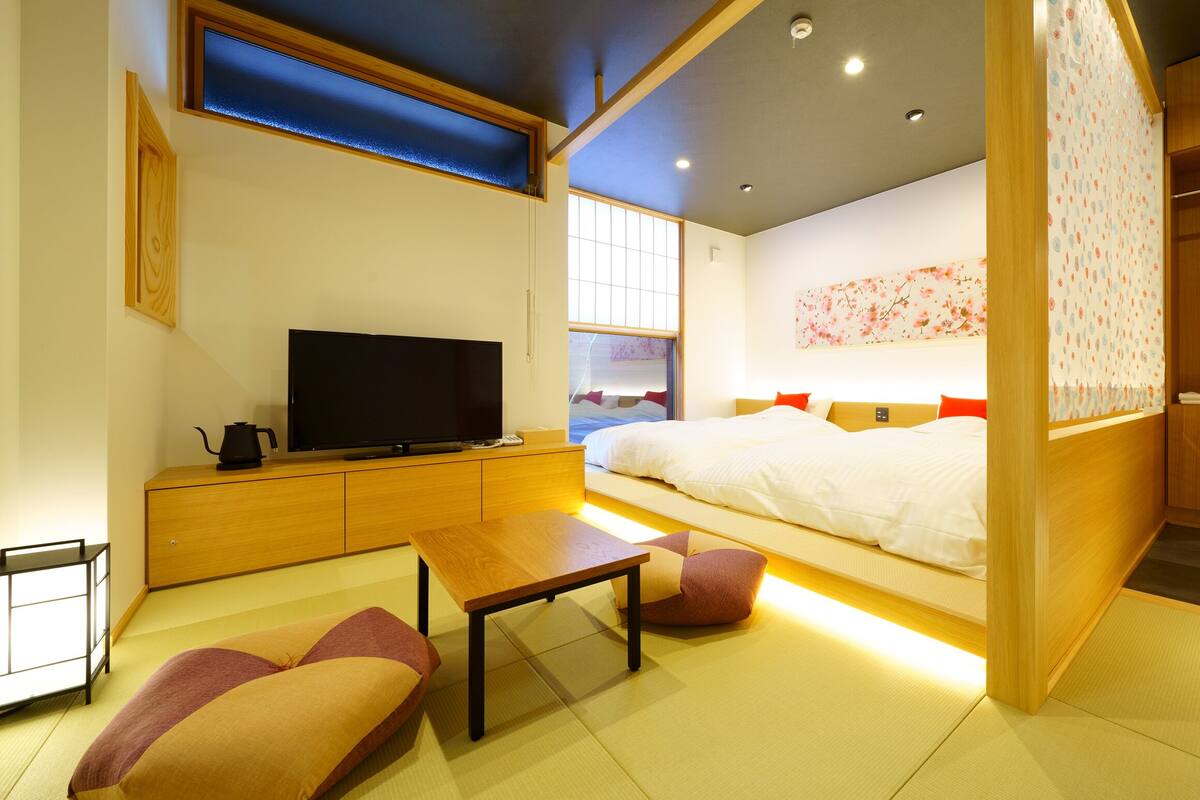 A modern hotel room with a bed, television, wooden furniture, and a view of the city.