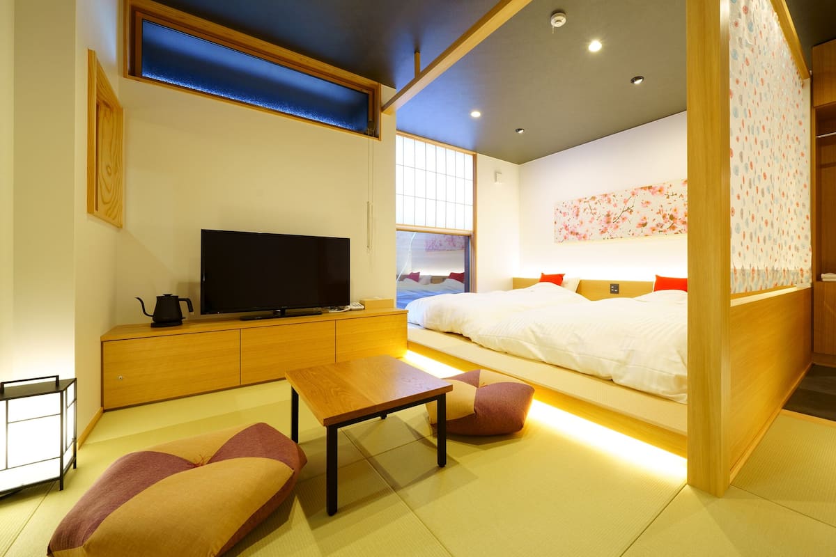 A modern hotel room with a bed, television, wooden furniture, and a view of the city.