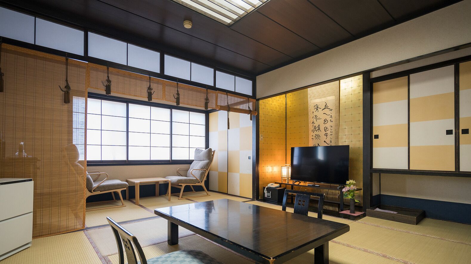 A traditional Japanese room with tatami flooring, a low table, chairs, a television, and sliding doors.
