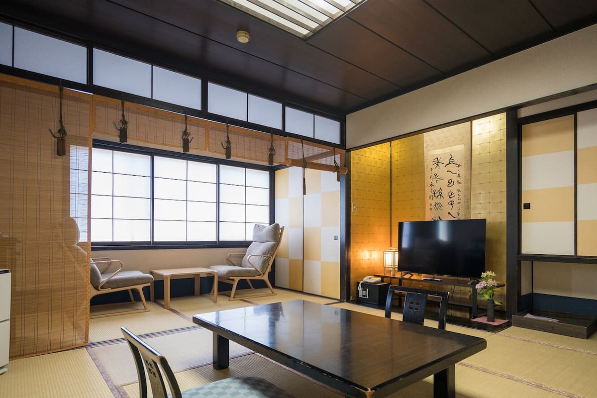A traditional Japanese room with tatami flooring, a low table, chairs, a television, and sliding doors.