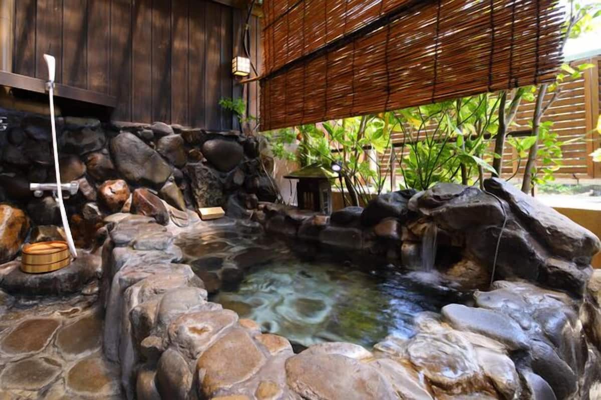 A stone hot spring bath area with a wooden structure, a stone basin, and a small waterfall.