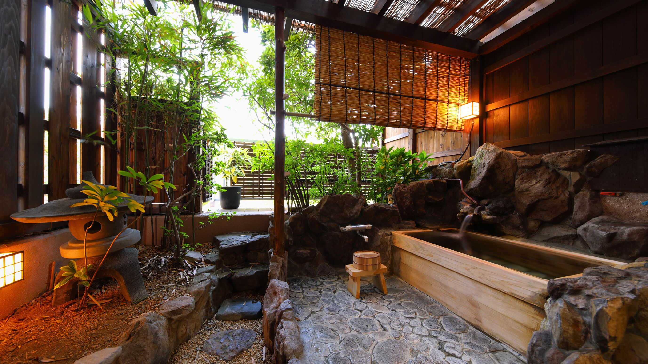 A traditional Japanese garden with a wooden bath, stone steps, bamboo, and a rock wall.