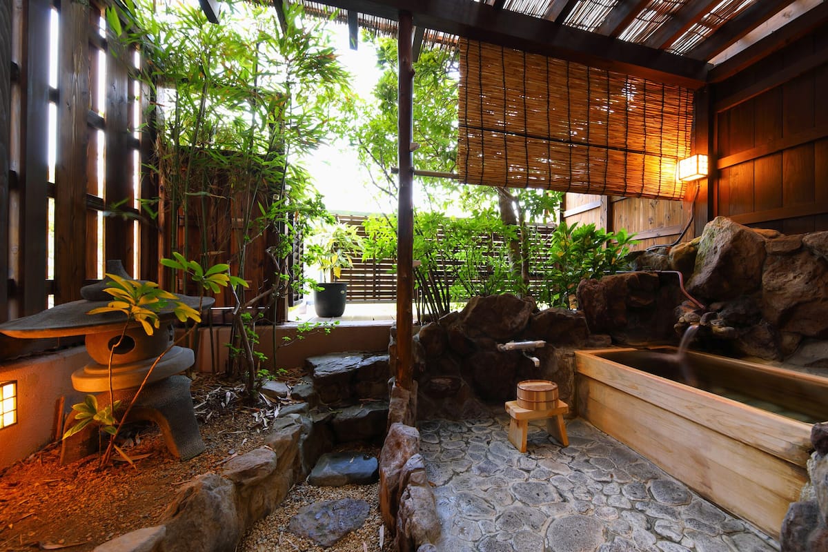 A traditional Japanese garden with a wooden bath, stone steps, bamboo, and a rock wall.