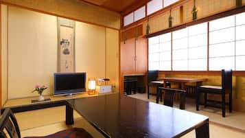 Una habitación japonesa tradicional con suelo de tatami, una mesa baja, sillas, un televisor y un biombio shoji.