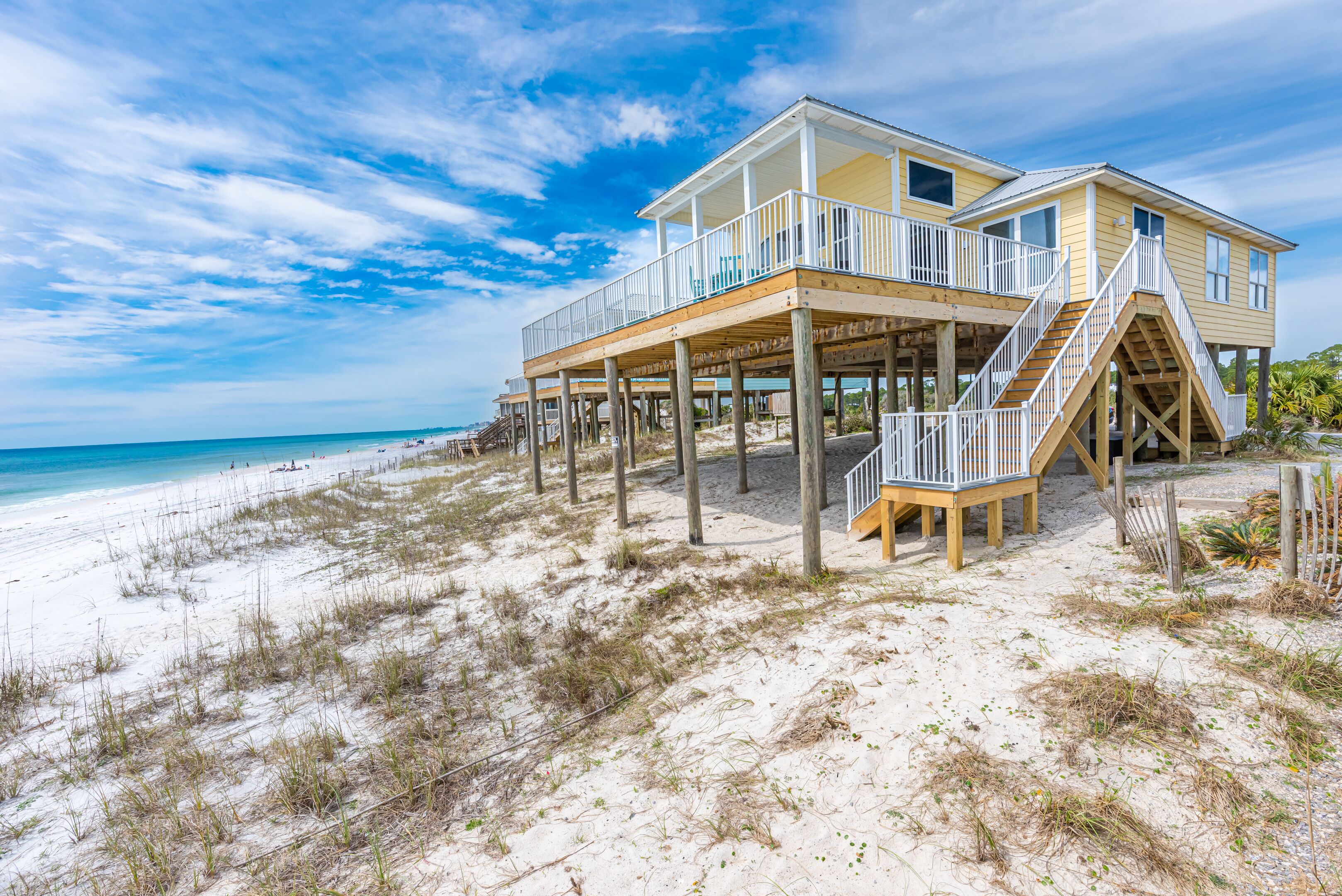 A beachfront house with a wooden deck and a staircase leading to a balcony.