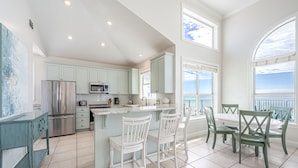A spacious kitchen with a central island, white bar stools, and a dining table with chairs.