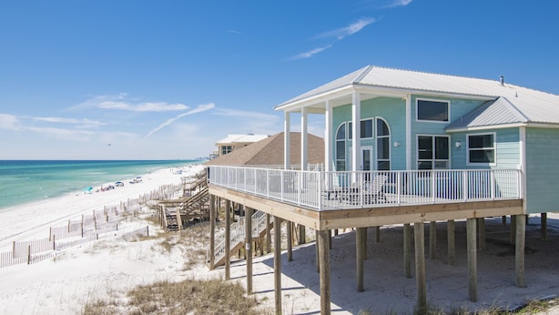 A beach house with a balcony, wooden deck, and a view of the ocean.