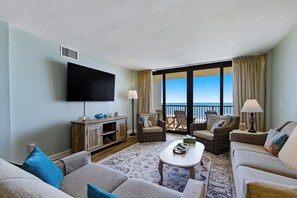 A living room with a flat-screen TV, wicker furniture, a coffee table, and a view of the ocean. - 🌟Oceanfront | Awesome Amenities | Great Views | Carolina Dunes 503🌟 (Myrtle Beach)