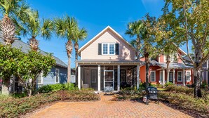 A two-story house with a covered porch, surrounded by palm trees and a brick pathway.