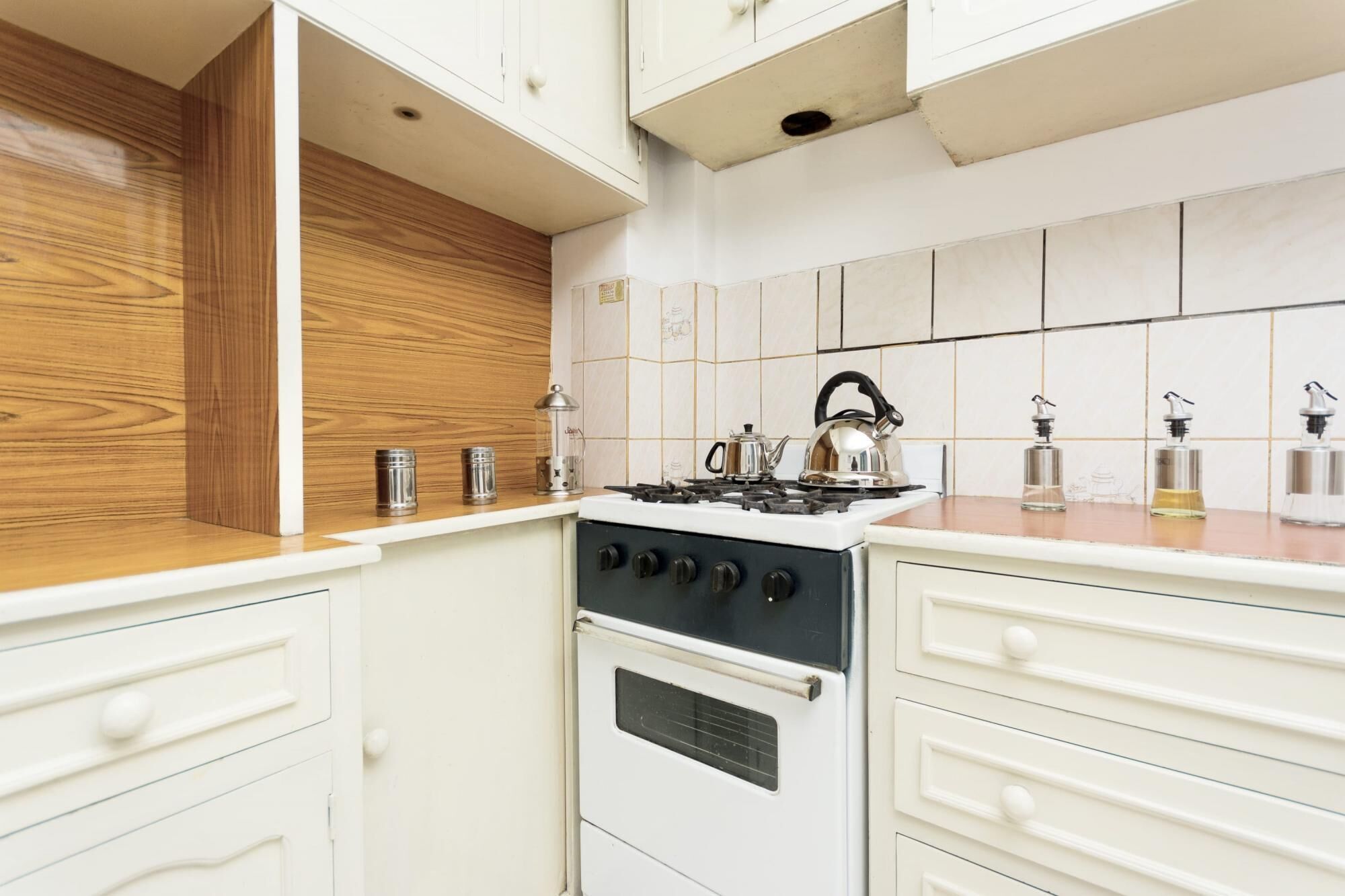 Een keuken met een witte kookplaat, houten spatwand en witte keukenkastjes.