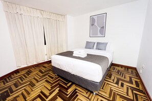Une chambre d’hôtel avec un lit, une fenêtre avec des rideaux, un sol à motifs et une œuvre d’art murale.