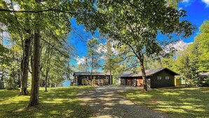 A rustic cabin-style lodging with a gravel driveway leading to a wooden deck and a small building. - Edgewater Retreat on Beautiful Soo Lake! (Phillips)