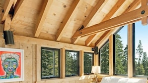 A wooden cabin bedroom with a bed, a painting, and large windows offering a forest view. - Amazing Architecture - Views all around VH#113 by Bear Valley Vacation Rentals (Arnold)