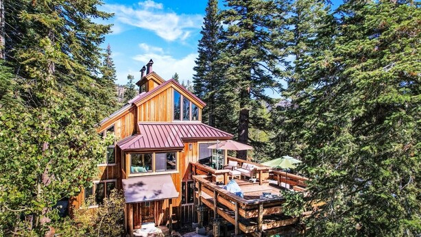 A wooden cabin with a deck and multiple windows, surrounded by dense forest. - Amazing Architecture - Views all around VH#113 by Bear Valley Vacation Rentals (Arnold)