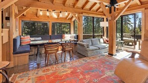 A cozy cabin interior with a wooden ceiling, large windows, a sofa, a dining table, and a patterned rug. - Amazing Architecture - Views all around VH#113 by Bear Valley Vacation Rentals (Arnold)