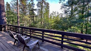 A wooden deck with chairs and a railing overlooking a forested area.