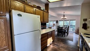 A kitchen with wooden cabinets, a refrigerator, a dining table with chairs, and a chandelier. - In the Pines, Cozy Retreat with Amazing Views (Idyllwild)