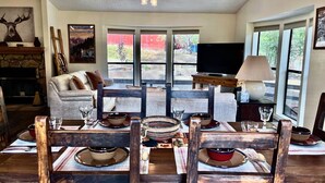 A dining area with a wooden table set for four, a fireplace, and a television in the background. - In the Pines, Cozy Retreat with Amazing Views (Idyllwild)