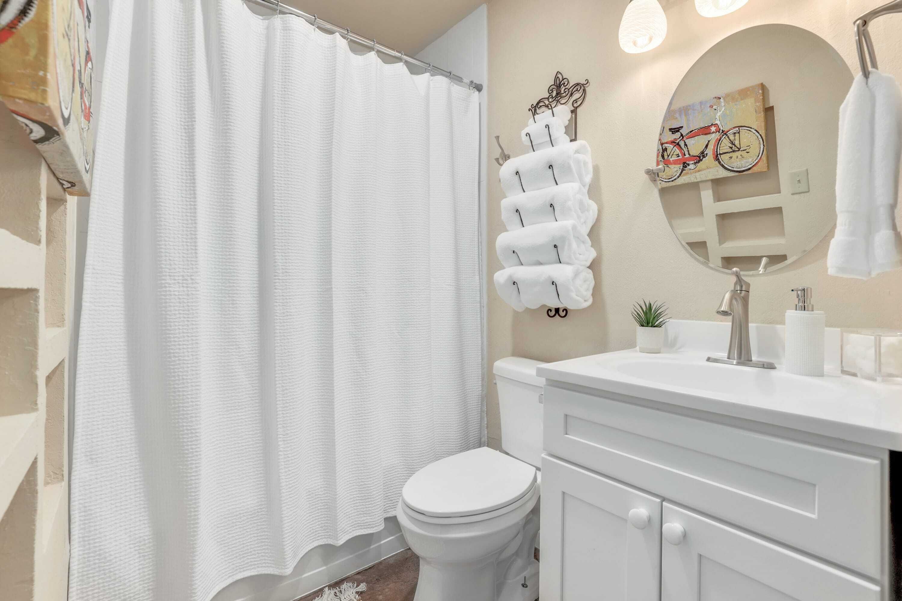 Ein Badezimmer mit Toilette, Waschbecken, Spiegel, Handtuchhalter und Duschvorhang.