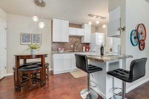A kitchen with white cabinets, a marble countertop, and a bar area with stools. - Market District Unit 1 - 1mi to DT Bentonville (Bentonville)