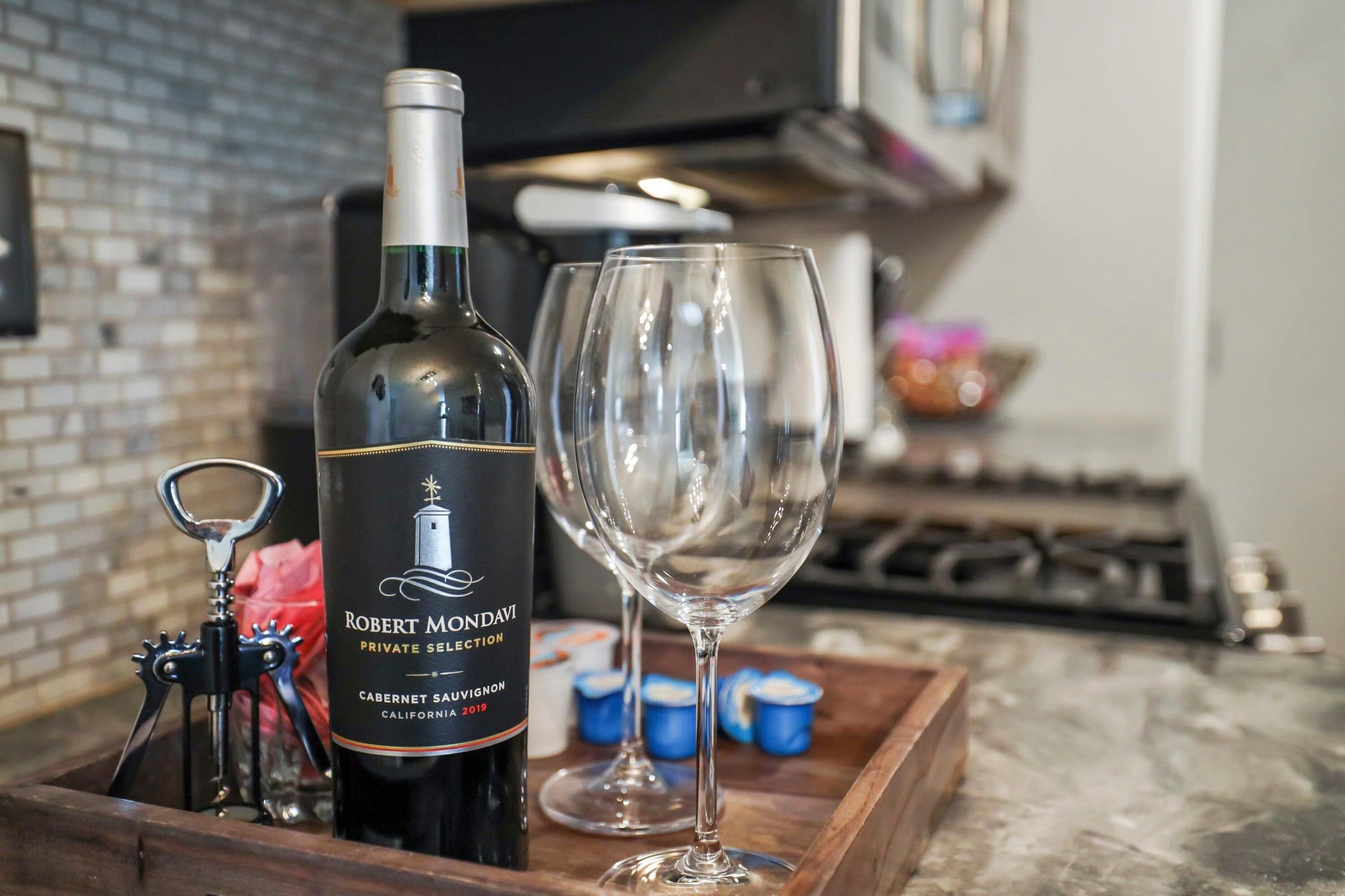 Eine Flasche Robert Mondavi Private Selection Cabernet Sauvignon, ein Flaschenöffner und ein leeres Weinglas auf einer Holzwasserliege.