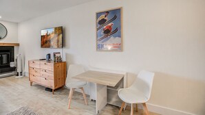 A modern living room with a wooden cabinet, two white chairs, a wooden table, and a mounted TV.