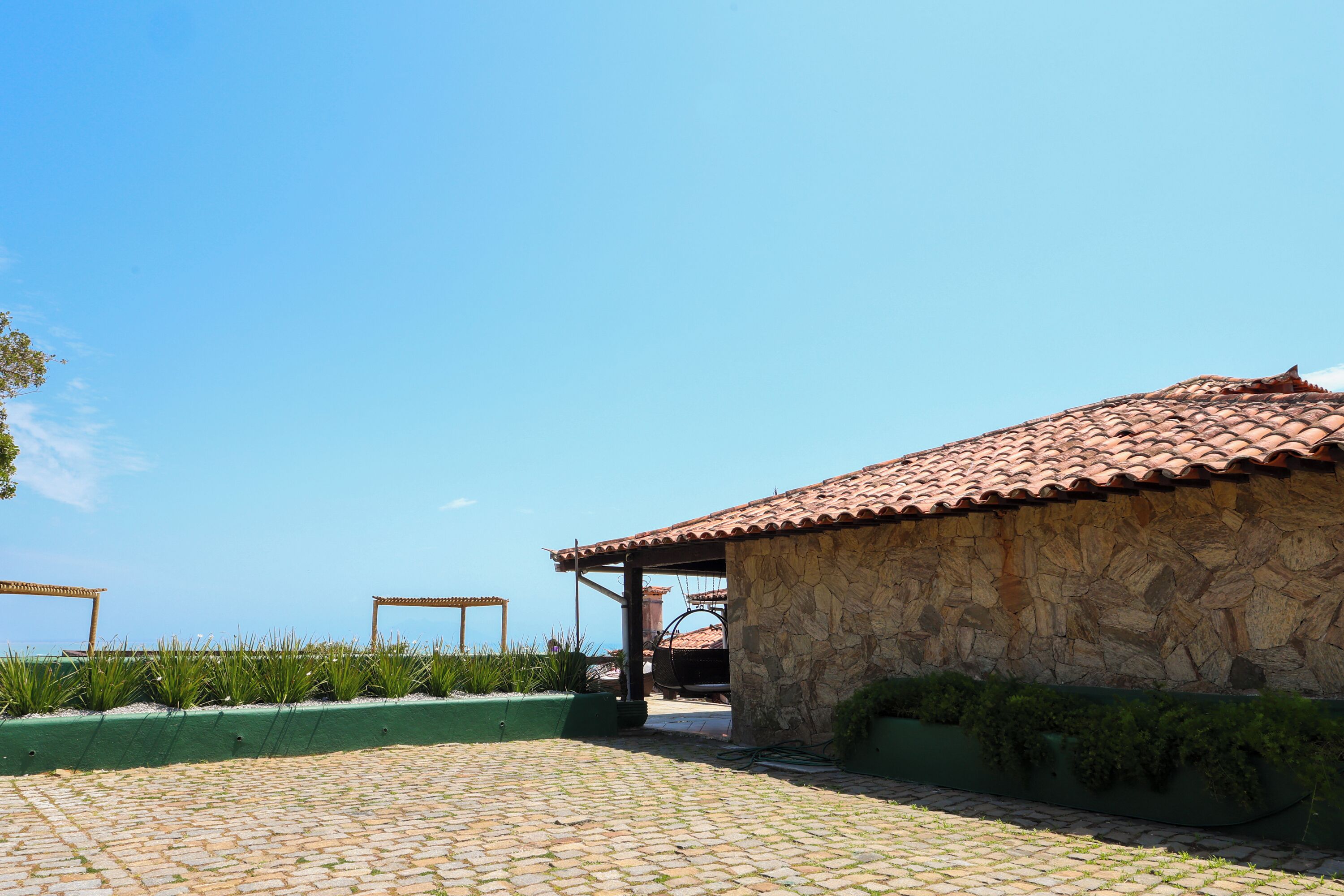 Um edifício de pedra com telhado em tijolos, um pátio pavimentado e vista para o mar.