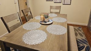 Una mesa de comedor con cuatro sillas, un centro de mesa y tres obras de arte enmarcadas en la pared.