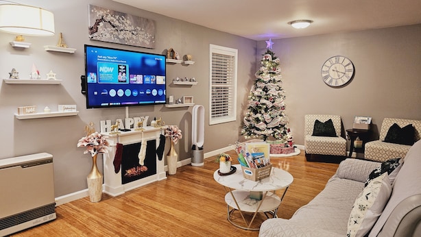 Una sala de estar con chimenea, un árbol de Navidad, un televisor de pantalla plana y un reloj en la pared.