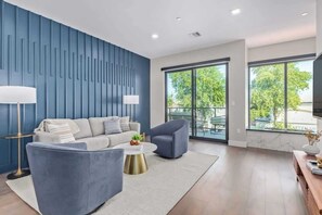Ein modernes Wohnzimmer mit blauer Akzentwand, einem Sofa, einem Sessel, einem Couchtisch und einem großen Fenster mit Blick ins Freie.