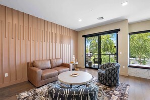 A modern living room with a sofa, armchair, and coffee table, large windows with a view of greenery, and a patterned rug.