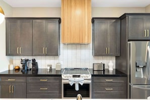A modern kitchen with dark cabinets, a central stove, and a refrigerator.