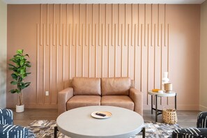 A modern living room with a sofa, a coffee table, a potted plant, and a side table with a lamp and decorative items.
