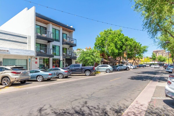 Vista callejera con coches aparcados, un edificio con balcones y árboles.
