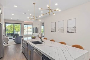 Eine moderne Küche mit einer Marmorinsel, Pendelleuchten und Kunstwerken an der Wand.