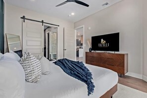 Ein Schlafzimmer mit Bett, Fernseher, Kleiderschrank und einer Schiebetür zum Badezimmer.